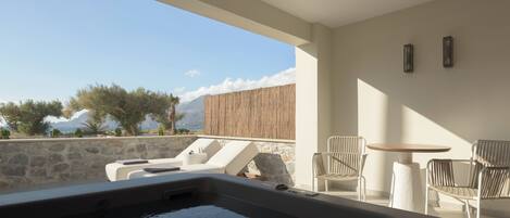 A modern outdoor hot tub area with lounge chairs and a table, overlooking a scenic landscape with mountains and trees.