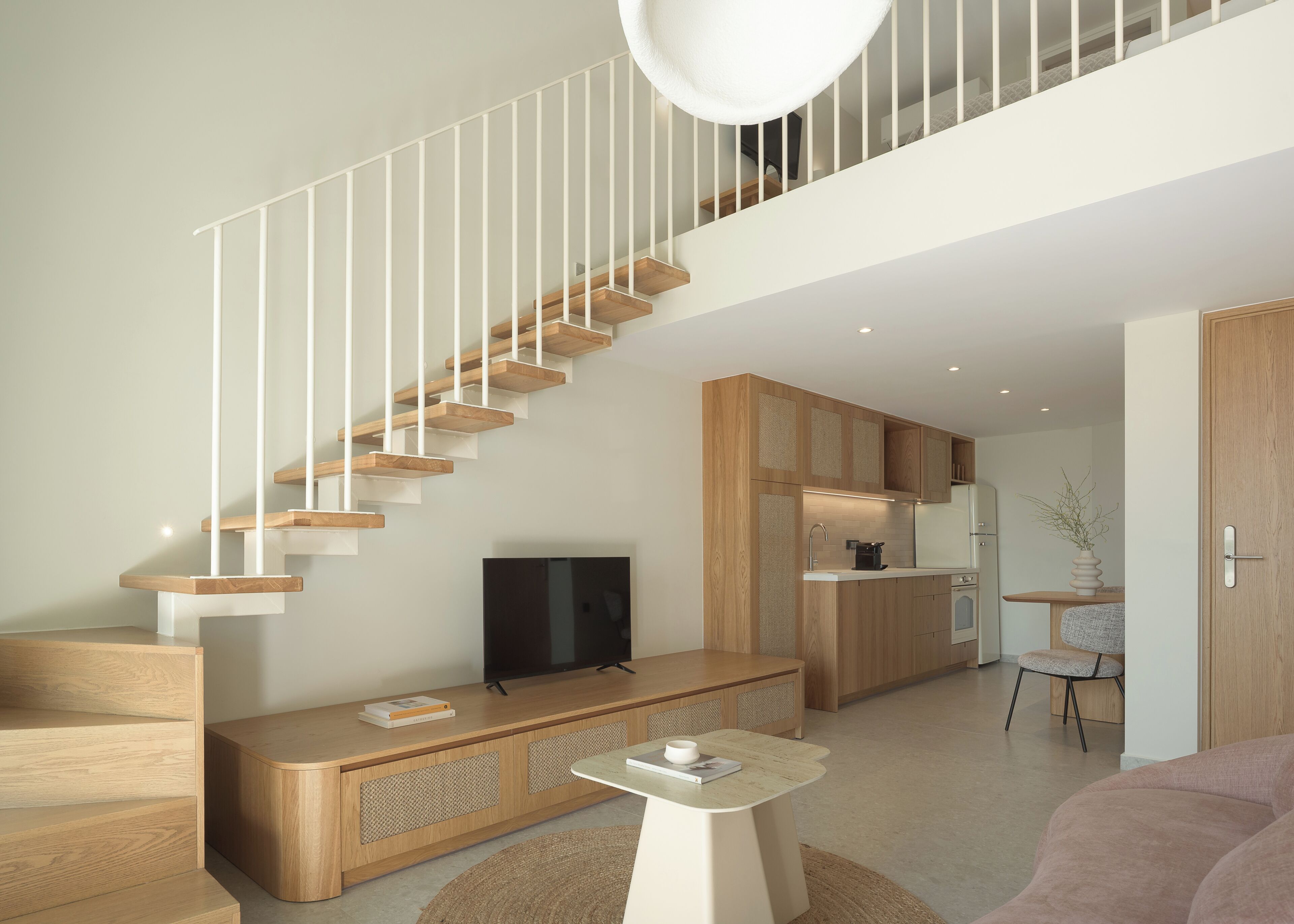 A modern interior with a wooden staircase, a flat-screen TV, a kitchen area, and a seating area with a coffee table.