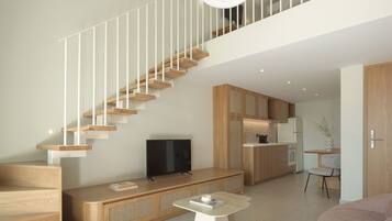 A modern interior with a wooden staircase, a flat-screen TV, a kitchen area, and a seating area with a coffee table.
