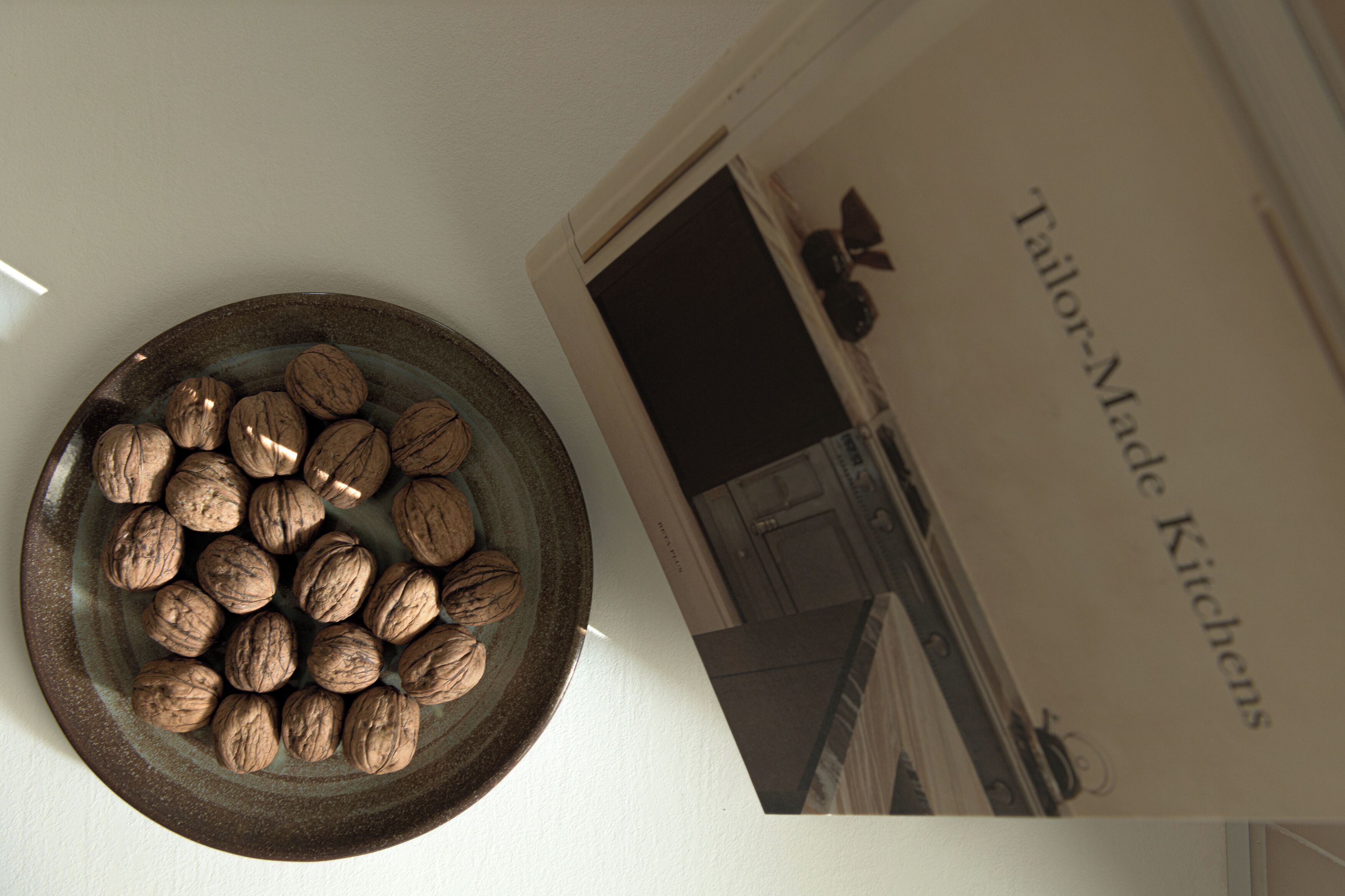A bowl of walnuts on a white surface next to a book titled "Tailor-Made Kitchens".