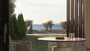 Ein moderner Balkon mit rundem Tisch und Stühlen, mit Blick auf eine Küstenlandschaft mit Zaun und Bäumen.