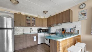 A modern kitchen with wooden cabinets, stainless steel appliances, and a glass island with stools. - New Listing!  Perfect retreat bayside off 28th St with a Pool! (Ocean City)