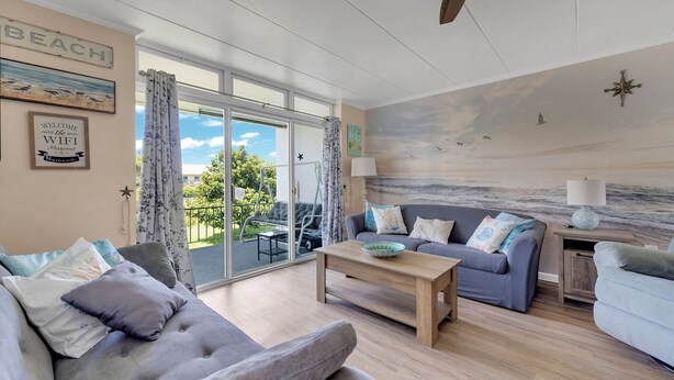 A spacious living room with a large sliding glass door leading to a balcony, a sofa, a coffee table, and a wall mural. - New Listing!  Perfect retreat bayside off 28th St with a Pool! (Ocean City)