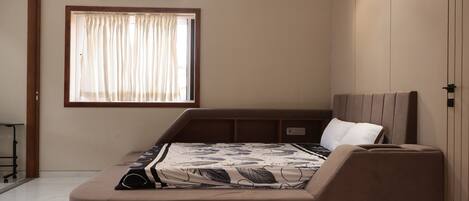 Un dormitorio con cama, ventana con cortinas, aire acondicionado y mesita de noche.