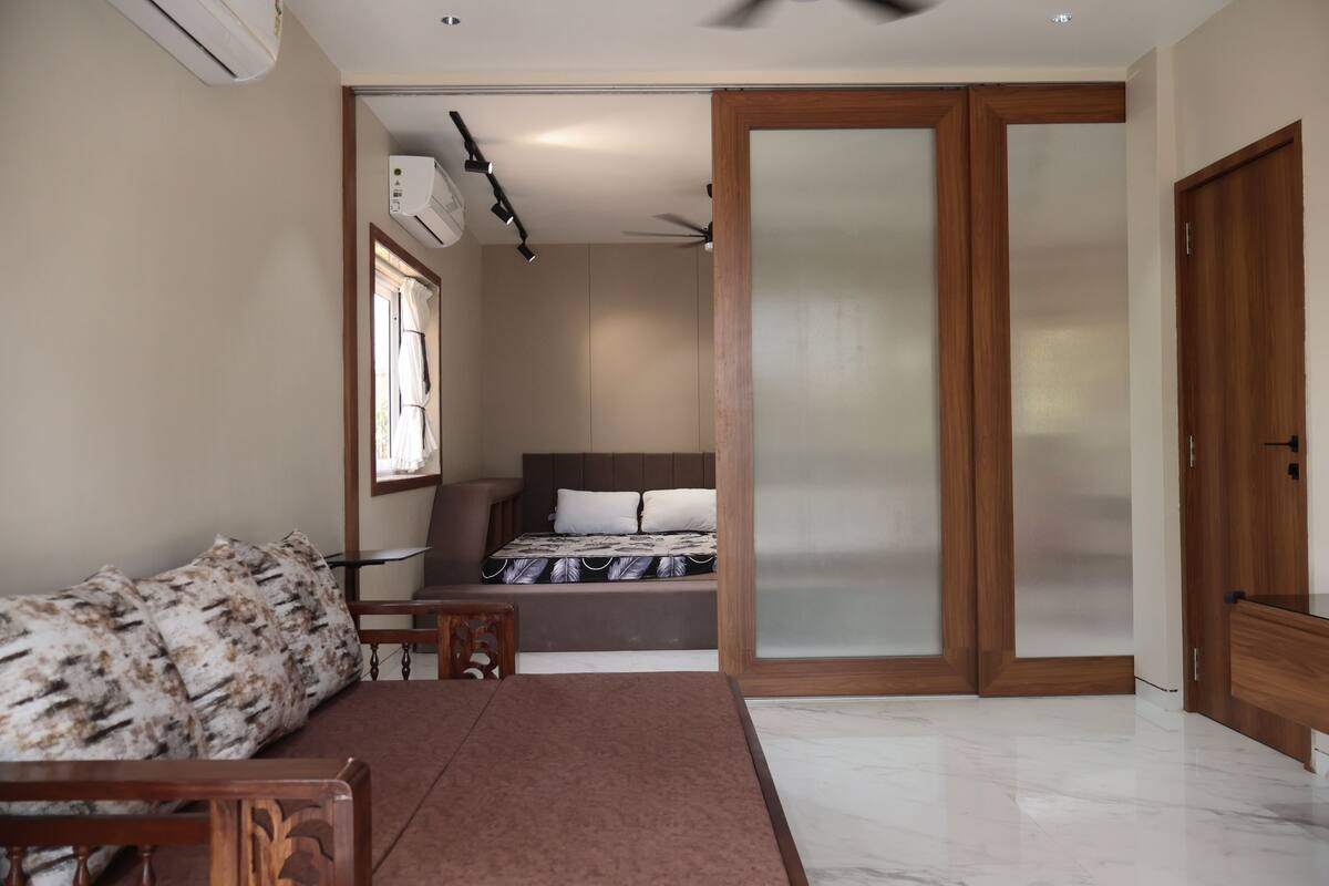 A bedroom with a bed, a wooden wardrobe, a window with curtains, and a ceiling fan.