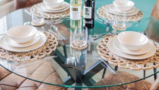A dining table set with white plates, silverware, and glassware, surrounded by brown leather chairs. - Comfortable home in Redcar (Redcar)