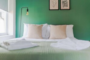 A neatly made bed with white linens and two pillows, a green wall, and a framed botanical print above it. - Comfortable home in Redcar (Redcar)