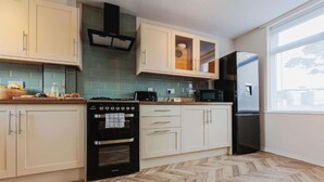 A modern kitchen with white cabinets, a black oven, a microwave, and a refrigerator. - Comfortable home in Redcar (Redcar)