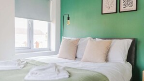 A neatly made bed with white linens and a green throw blanket, a bedside lamp, and two framed botanical prints on the wall. - Comfortable home in Redcar (Redcar)