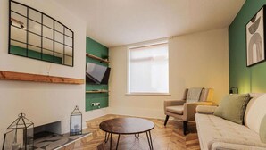 A modern living room with a herringbone floor, a round coffee table, a beige sofa, a green accent wall, and a large window. - Comfortable home in Redcar (Redcar)