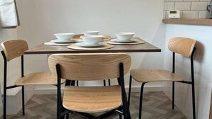 A dining area with a table set for four, surrounded by chairs, a wall-mounted mirror, and a light fixture.