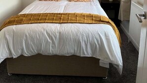 A neatly made bed with a patterned headboard, two framed artworks on the wall, and a window with curtains.