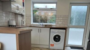 A compact kitchen with a built-in washing machine, a window with a view, and a herringbone-patterned floor.