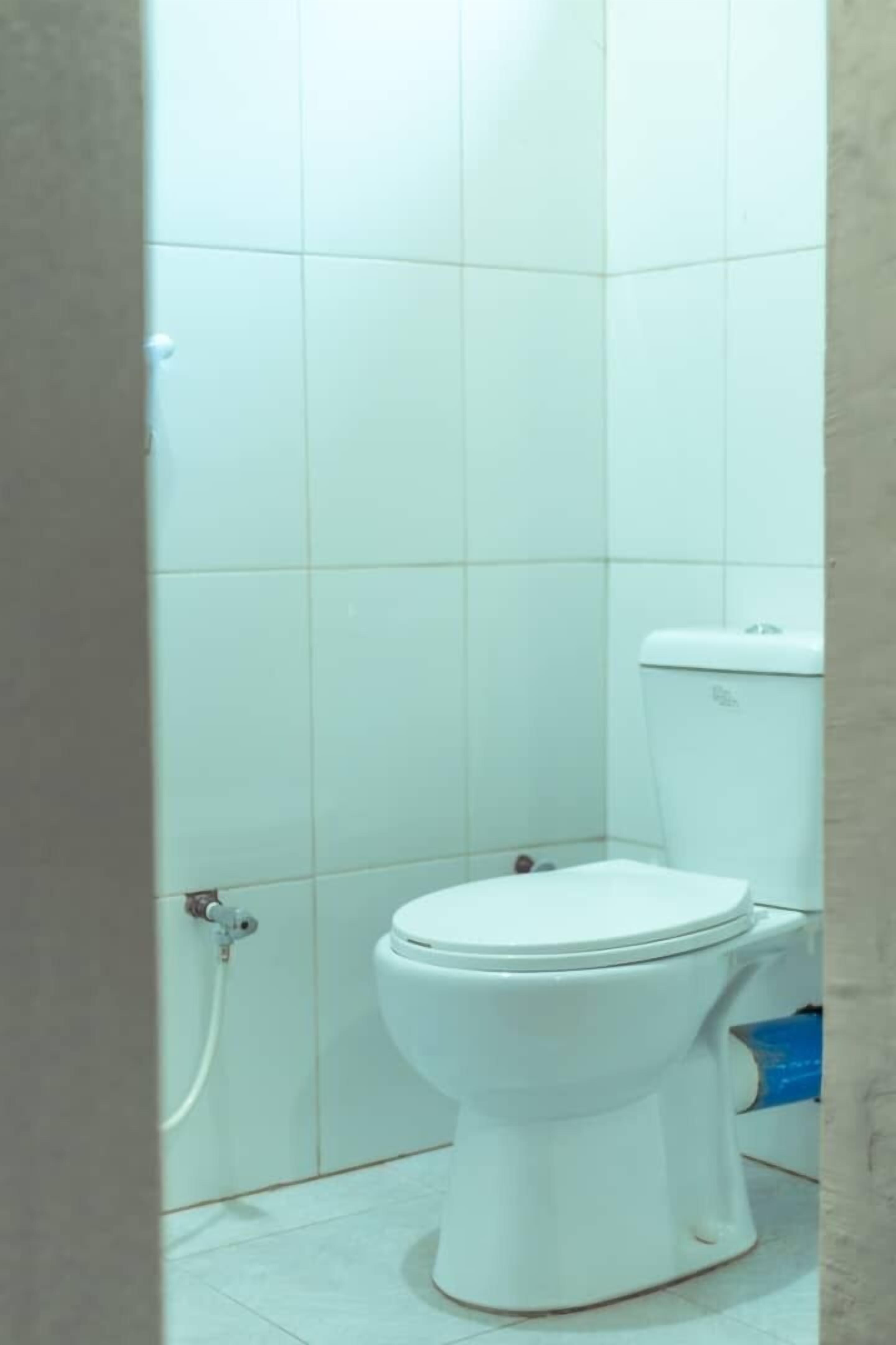A small, white toilet in a bathroom with white tiled walls and floor.