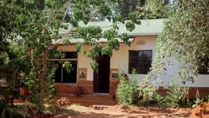 A rustic building with a green roof, surrounded by lush greenery and a dirt path leading to the entrance. - Kilimanjaro sons Homestay (Moshi)