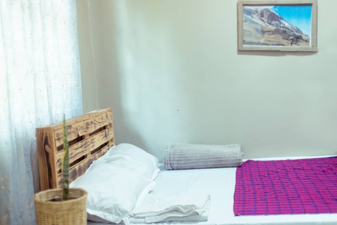A bed with a wooden headboard, a white pillow, a folded blanket, and a red patterned blanket.