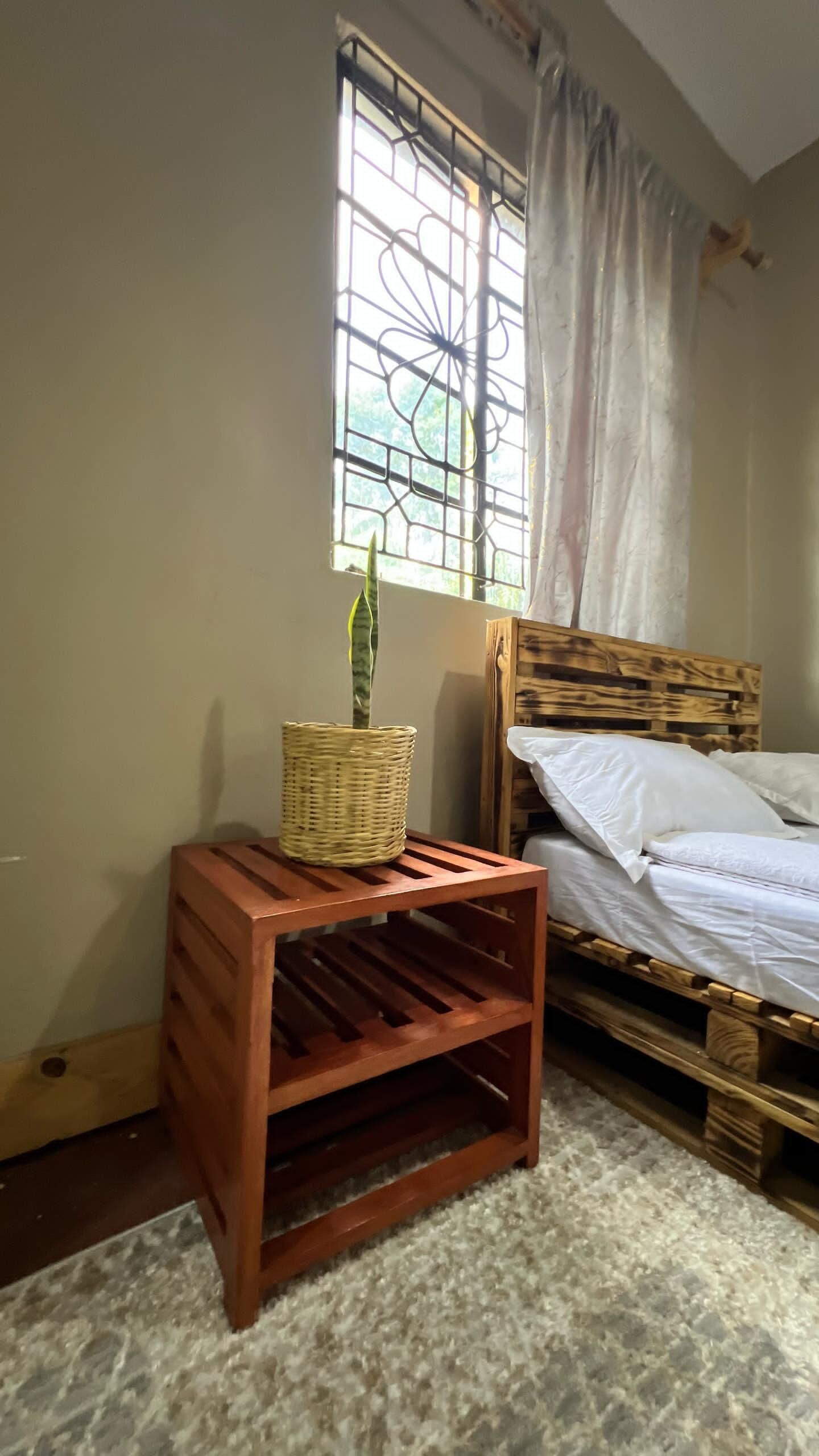 Une chambre à coucher avec un lit, une table de chevet en bois, un panier en osier et une fenêtre donnant sur un paysage verdoyant.