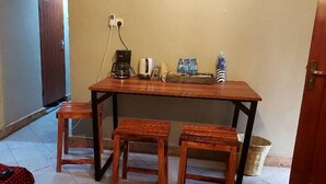 A small wooden table with two matching stools, a coffee maker, a toaster, and a basket of bottled water. - Kilimanjaro sons Homestay (Moshi)