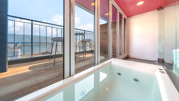 Ein modernes Badezimmer mit einer gläsernen Whirlwanne, einer Holzterrasse und Meerblick.