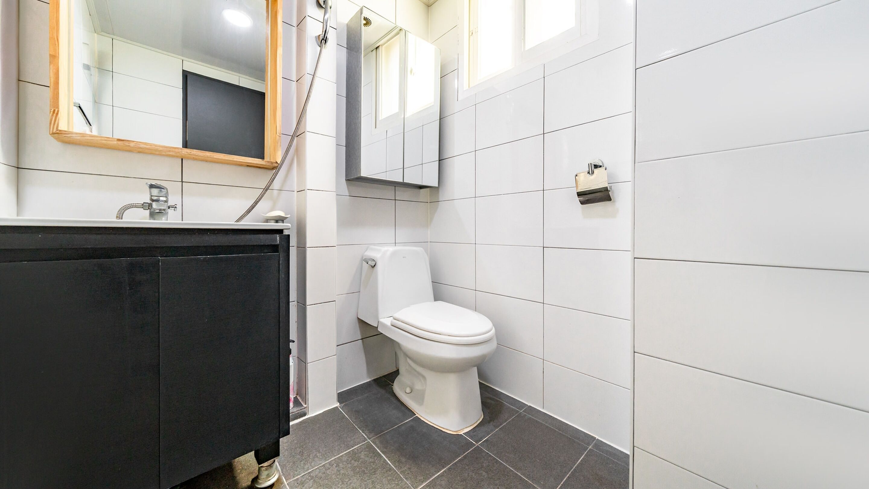 A modern bathroom with a black vanity, white toilet, and tiled walls.