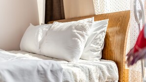 Ein ordentlich bezogenes Bett mit weißen Leinen und Kissen, ein hölzerner Kopfteil und ein durchsichtiges Spitzenfenster sind zu sehen.