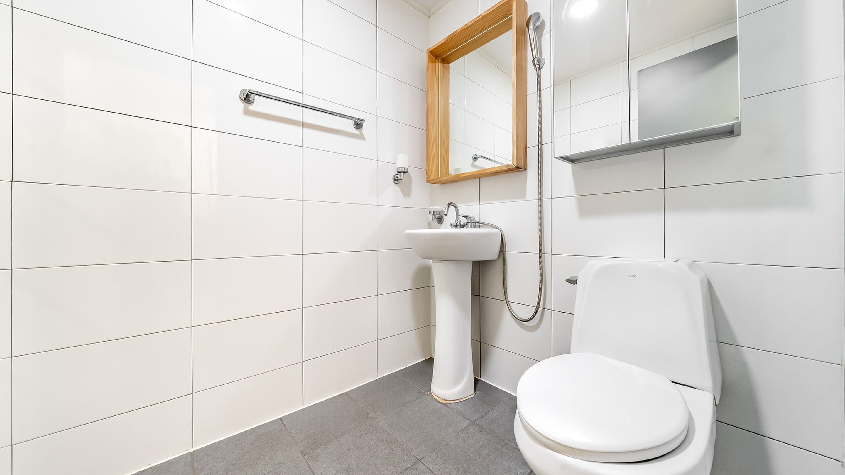 A modern bathroom with white tiles, a white sink, a toilet, and a shower.