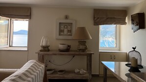 A cozy room with a bed, a wooden table with a lamp, a framed picture, and a view of the sea. - In the heart of Poros, stunning panoramic views, privacy and serenity. (Poros)