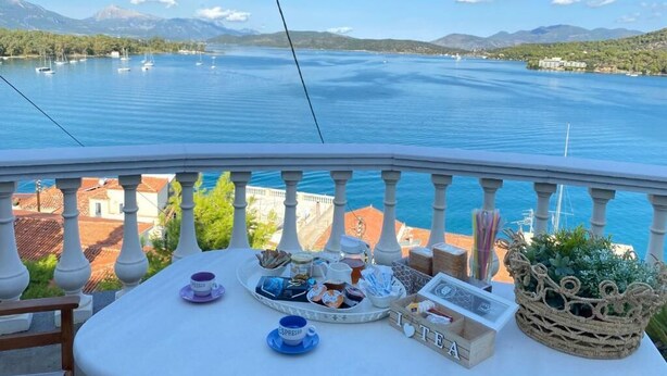 A balcony with a table set for tea, overlooking a lake with boats and mountains in the background. - In the heart of Poros, stunning panoramic views, privacy and serenity. (Poros)