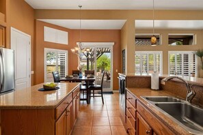 Una cocina con una isla central, un lavamanos doble, armarios de madera y una zona de comedor con mesa y sillas.