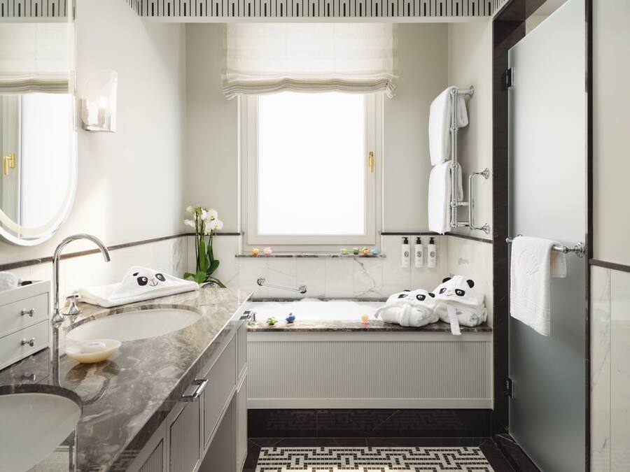 A modern bathroom with a vanity, sink, and bathtub. There are towels and toiletries on the counter.
