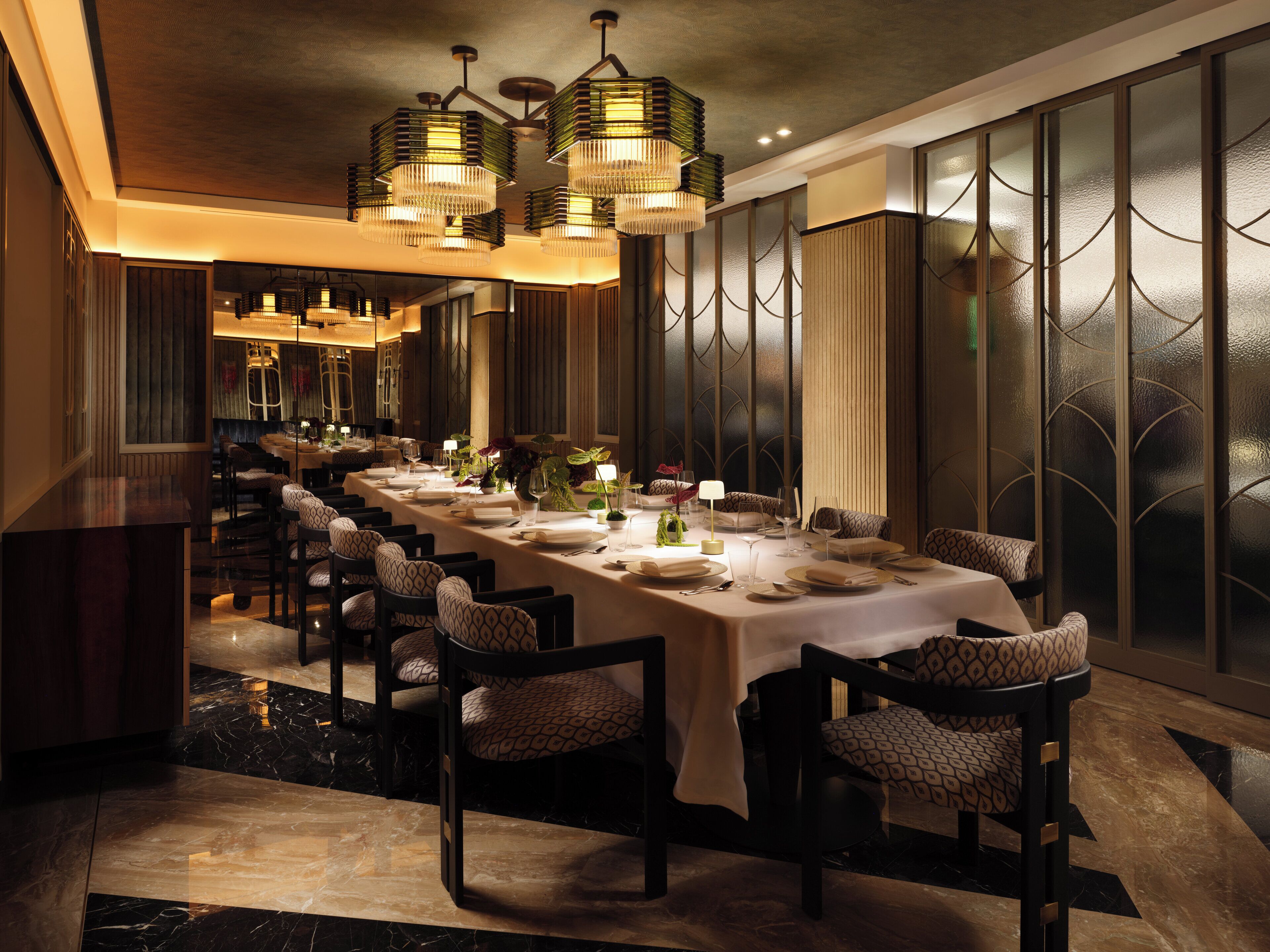 Mesa de jantar comprida posta para refeição, com várias cadeiras, luminárias elegantes e design de interiores moderno.