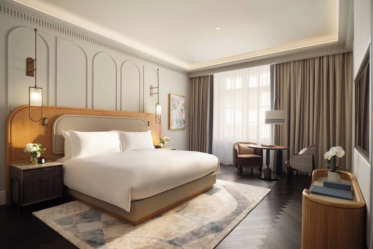Ein modernes Hotelzimmer mit einem großen Bett, einem Nachttisch mit Lampe, einem kleinen runden Tisch und einem Sessel.
