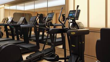 A gym with treadmills and elliptical machines, wooden floors, and a large mirror wall.