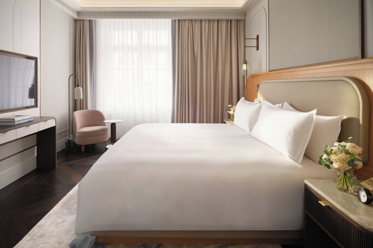 A hotel room with a large bed, a desk, a chair, a TV, and a nightstand with a clock.