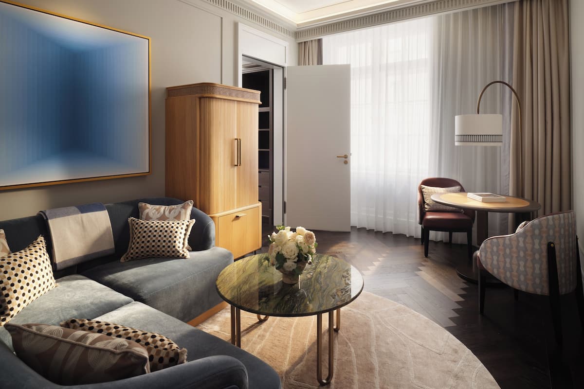 Ein modernes Hotelzimmer mit Sofa, einem Glastisch, einem Esstisch und einem Kleiderschrank.