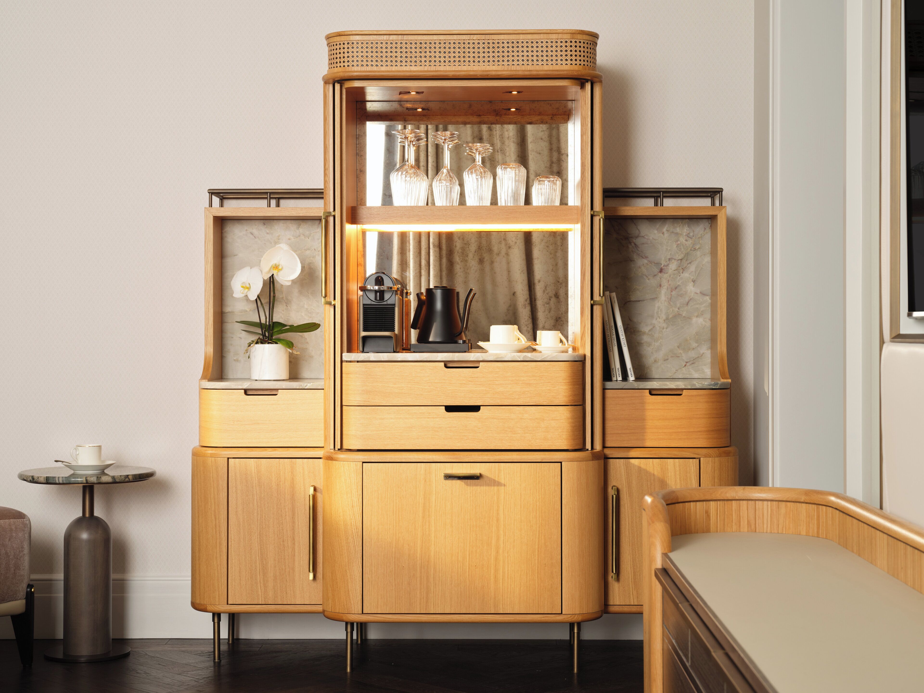A wooden cabinet with a glass front, drawers, and shelves, containing a coffee maker, cups, and decorative items.