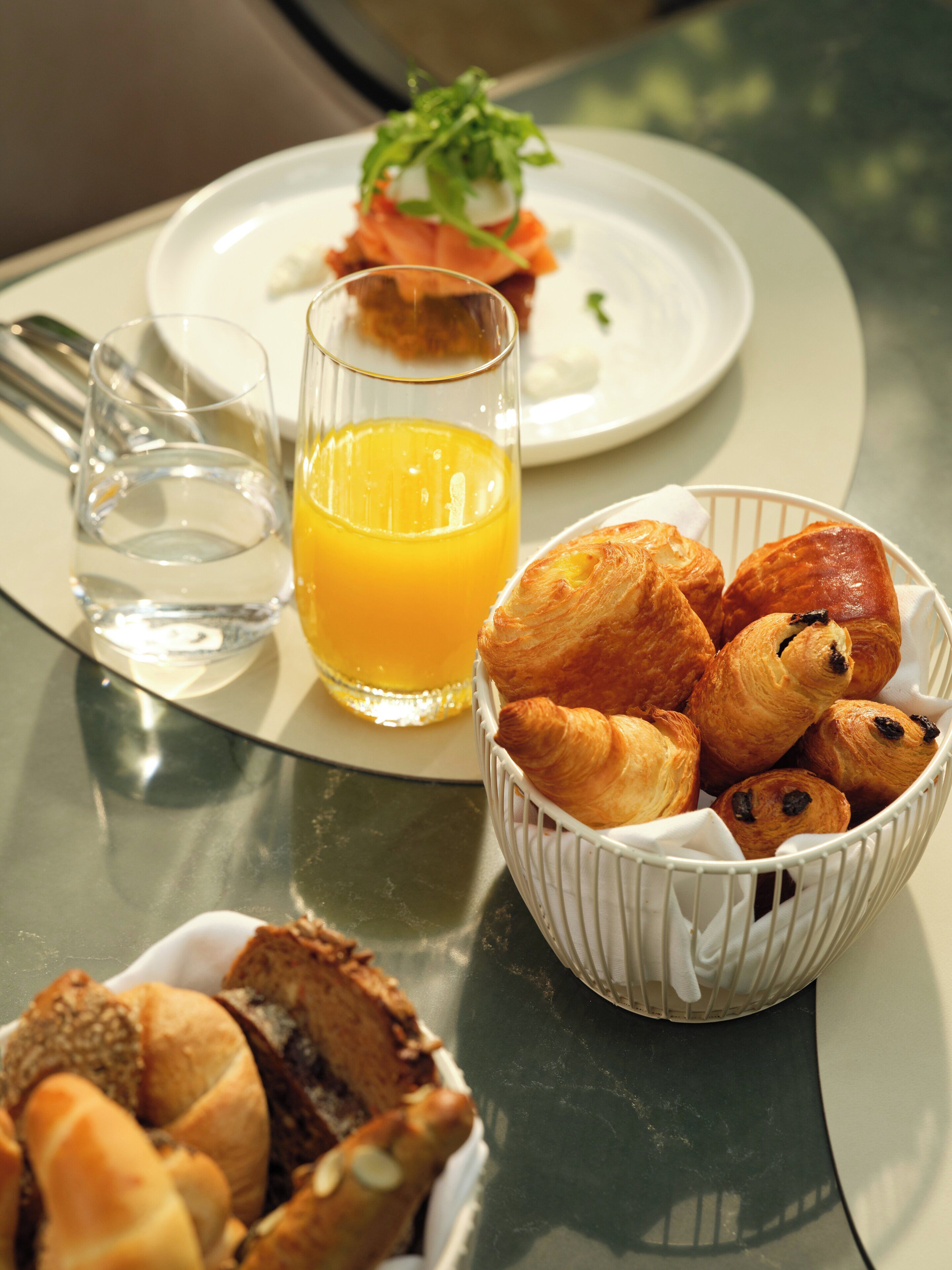 Une table avec des croissants, un verre de jus d’orange et une assiette de nourriture.