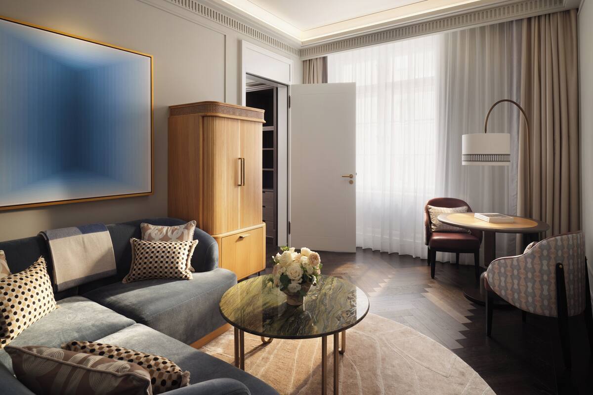 A modern hotel room with a sofa, a glass coffee table, a dining table, and a wardrobe.