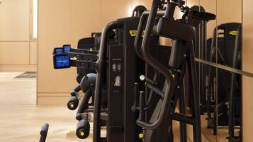 Uma academia com diversos equipamentos de exercício, uma tela digital e piso de madeira.