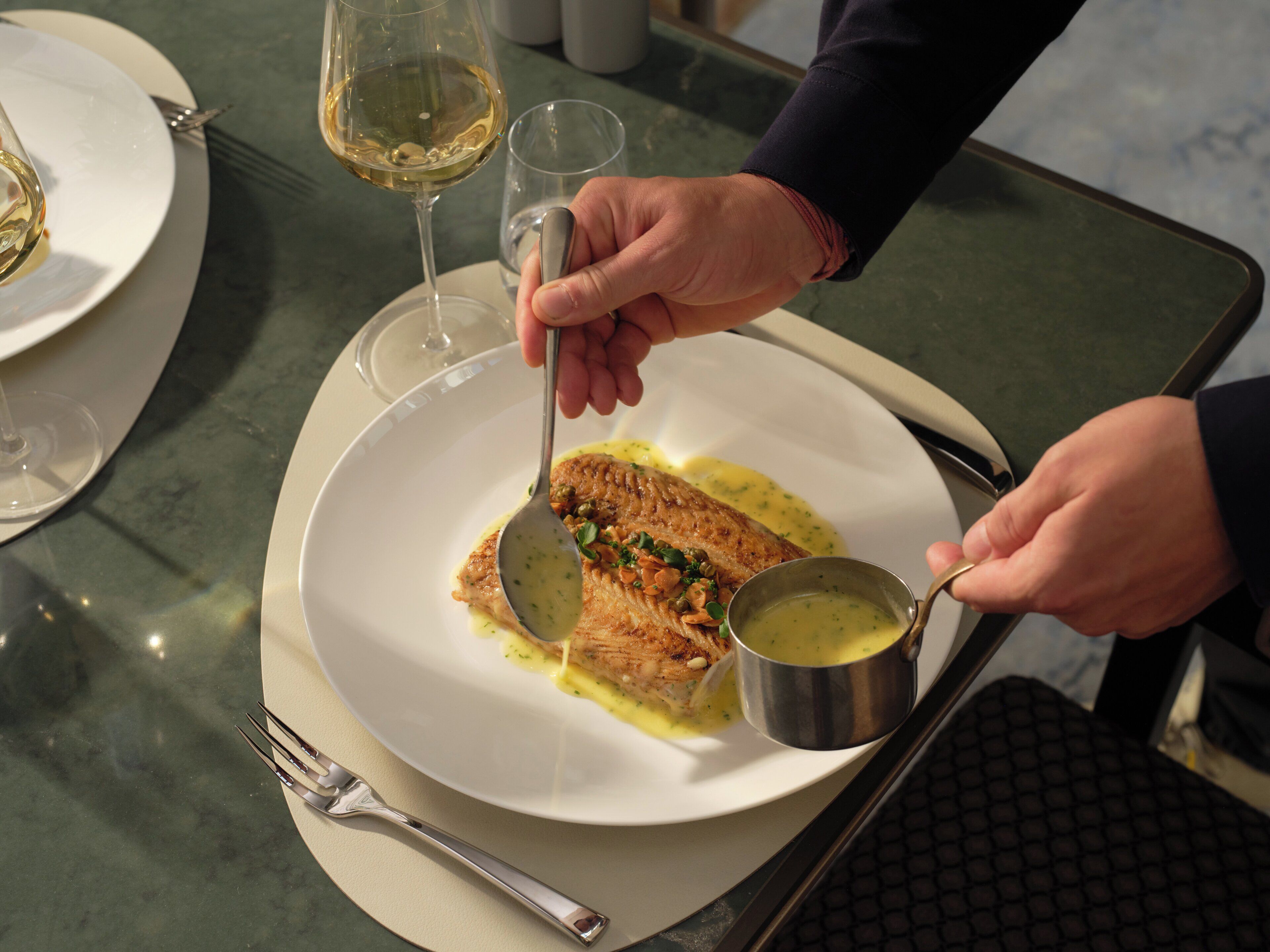 Uma mesa de jantar com um prato de comida, um copo de vinho branco e uma caneca de metal.