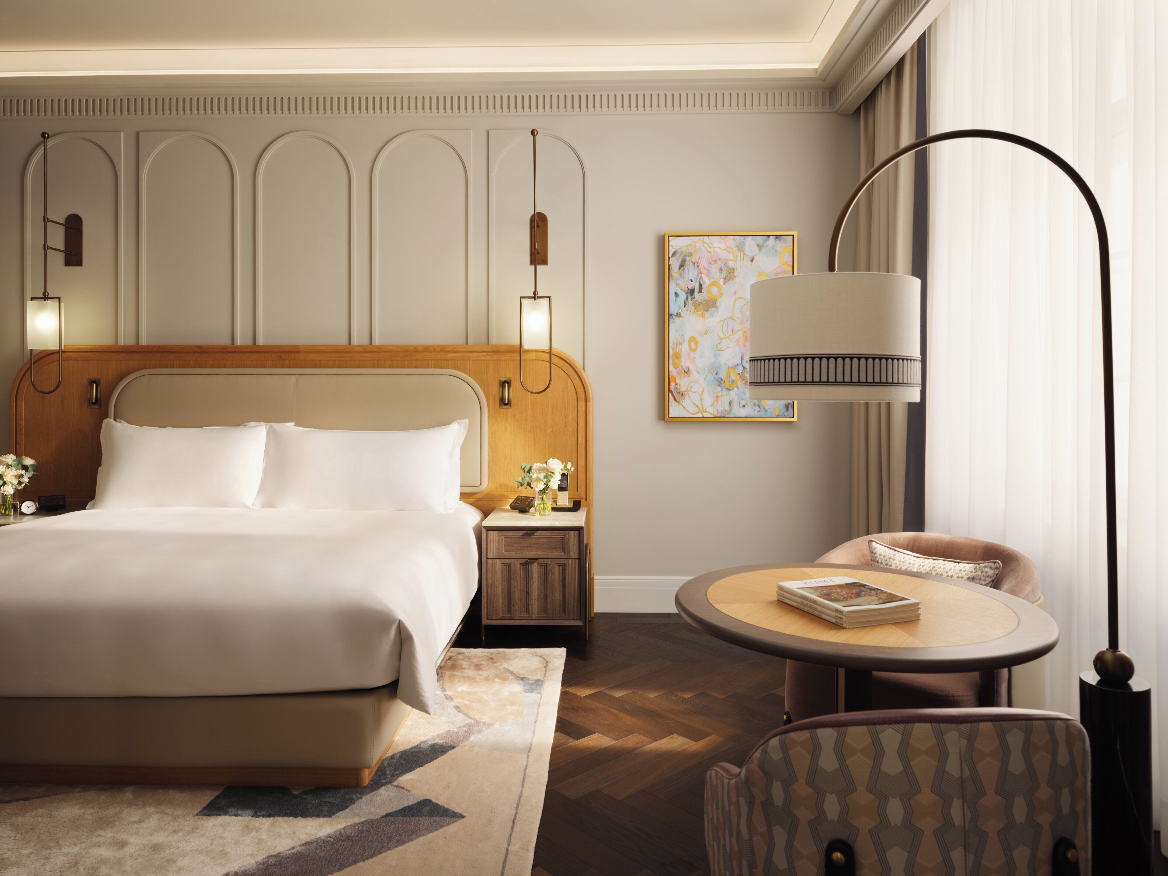 Une chambre d’hôtel avec un grand lit, des tables de chevet, une table ronde avec une chaise et une lampe sur pied.
