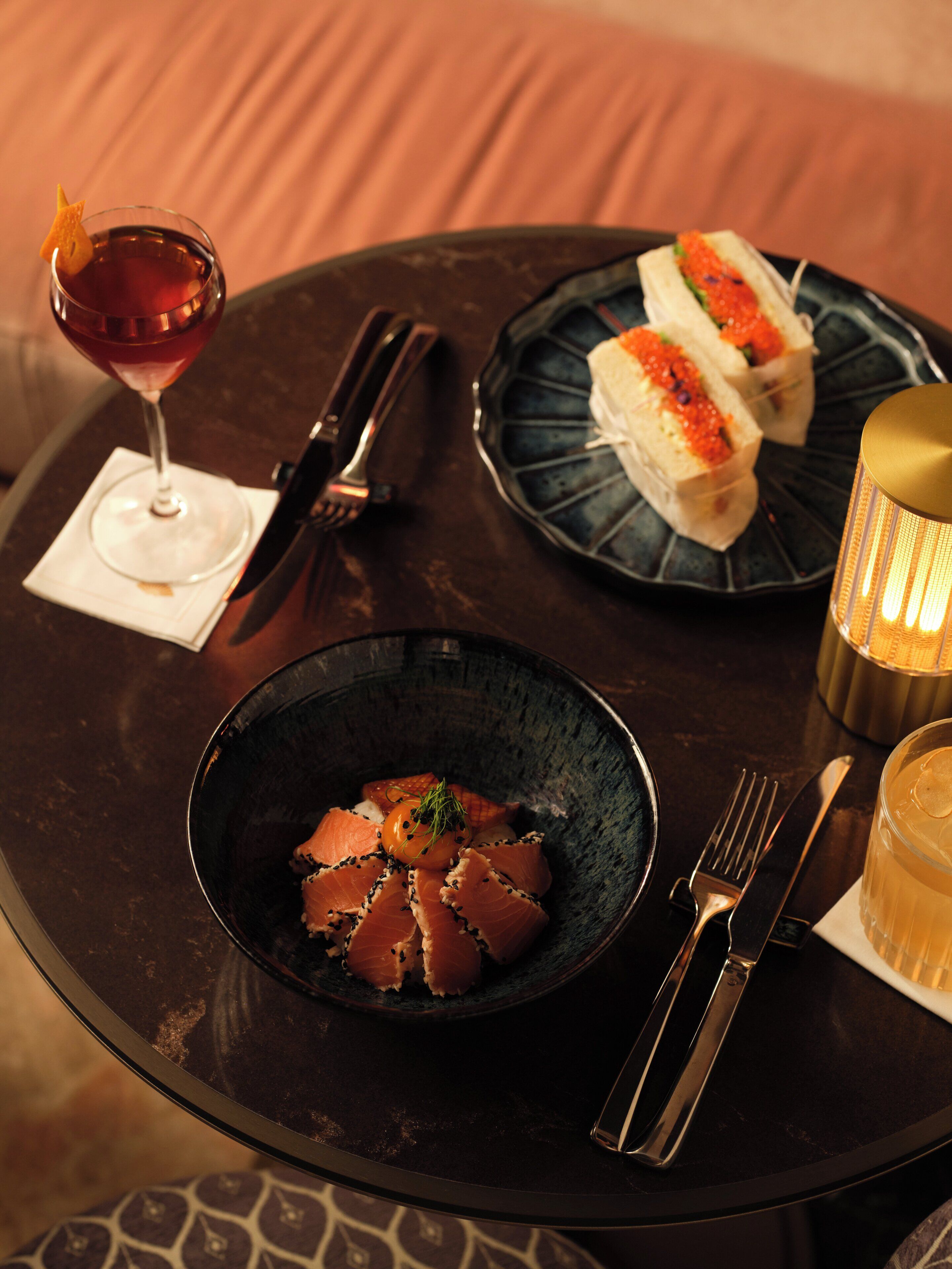 Une table dressée avec un verre à martini, un bol de sashimi, une assiette de sushis et une bougie.