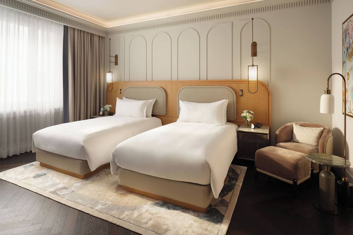 Ein Hotelzimmer mit zwei Betten, einer Sitzecke mit einem Sessel, einem Nachttisch und einer Lampe.