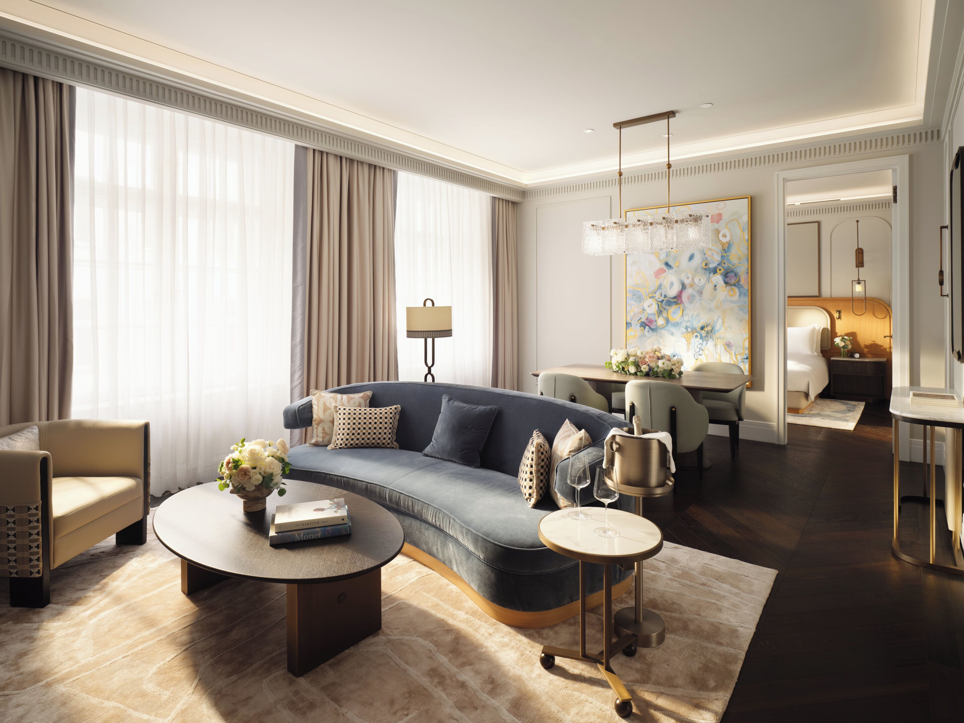 A modern living room with a blue sofa, a round coffee table, and a dining area with a chandelier.