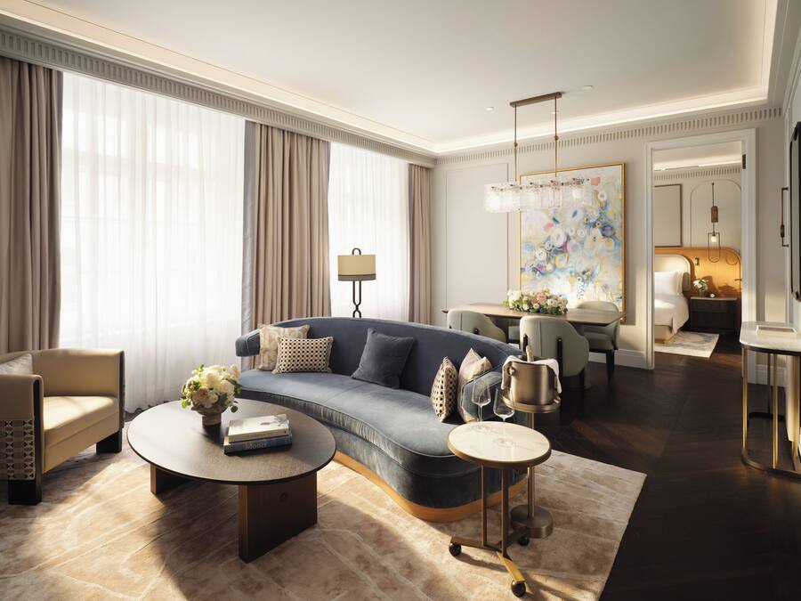 A modern living room with a blue sofa, a round coffee table, and a dining area with a chandelier.