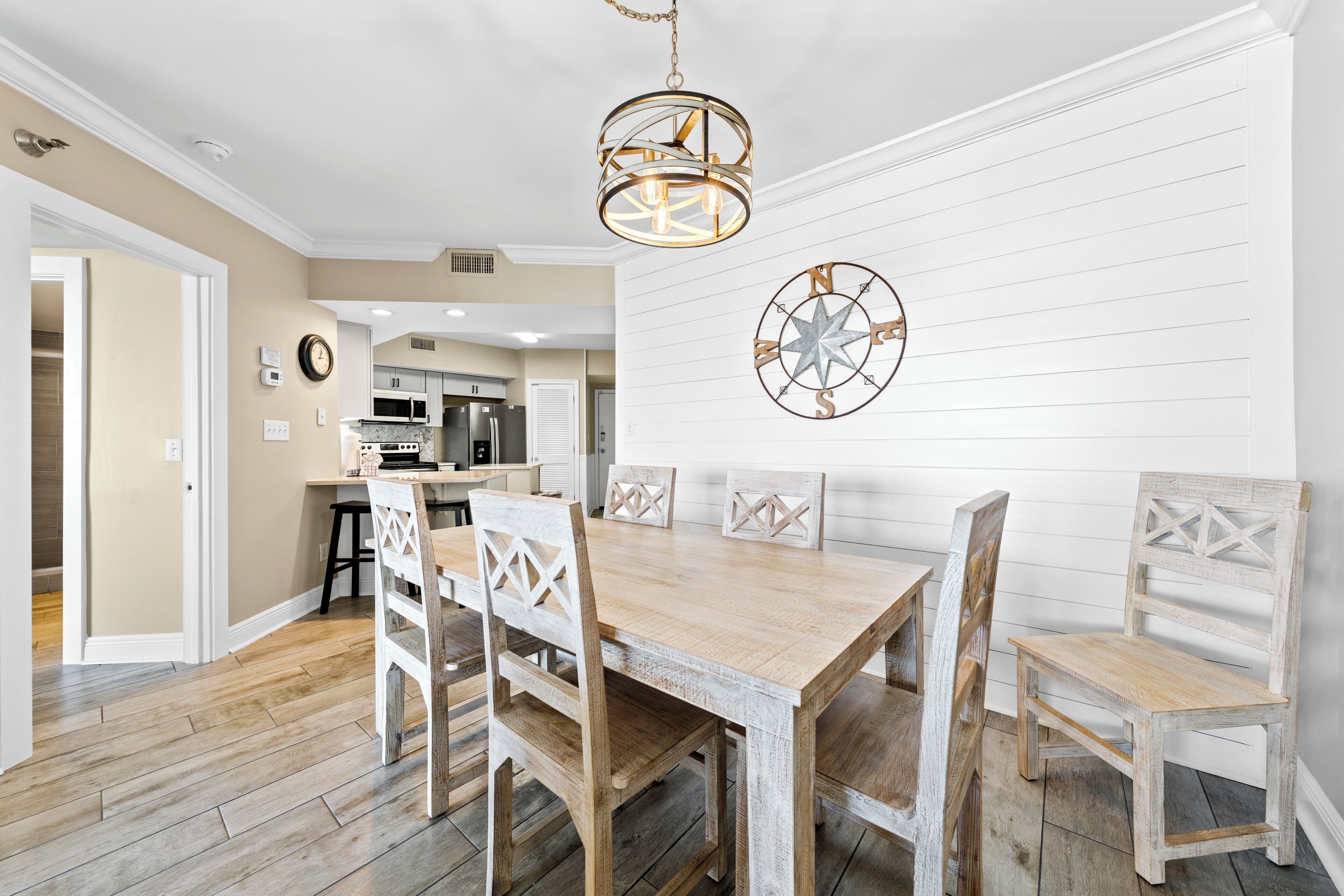 A dining area with a wooden table and chairs, a chandelier, and a compass wall decoration.