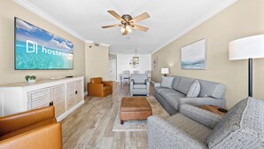 Un salon moderne comprenant un téléviseur, un canapé, des fauteuils et un ventilateur de plafond.