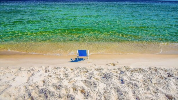 Une plage à l’eau turquoise et cristalline, avec une seule chaise longue bleue.
