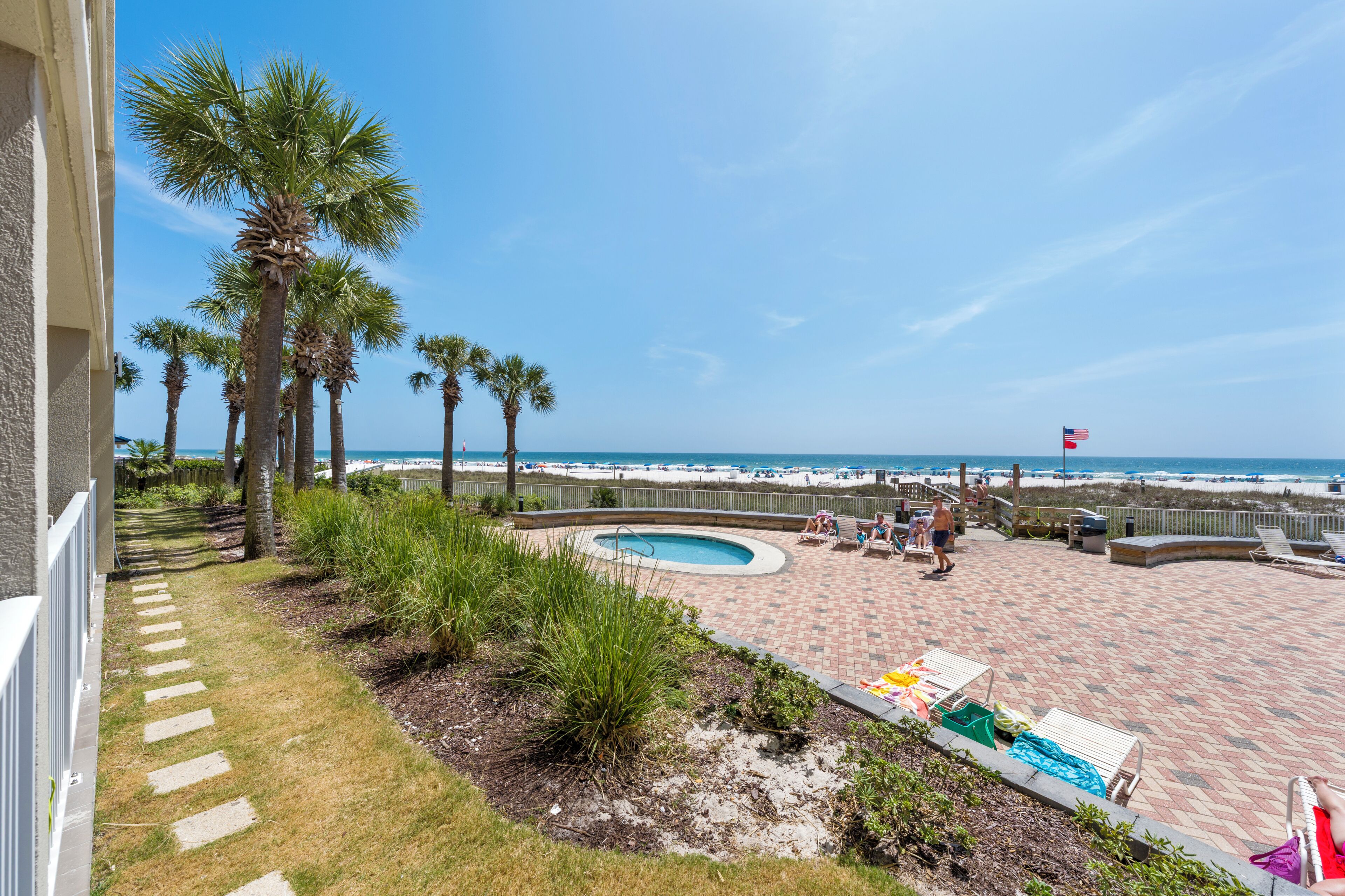 A pool area with lounge chairs and palm trees, overlooking a beach.