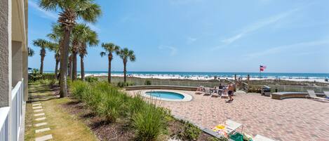 A pool area with lounge chairs and palm trees, overlooking a beach.
